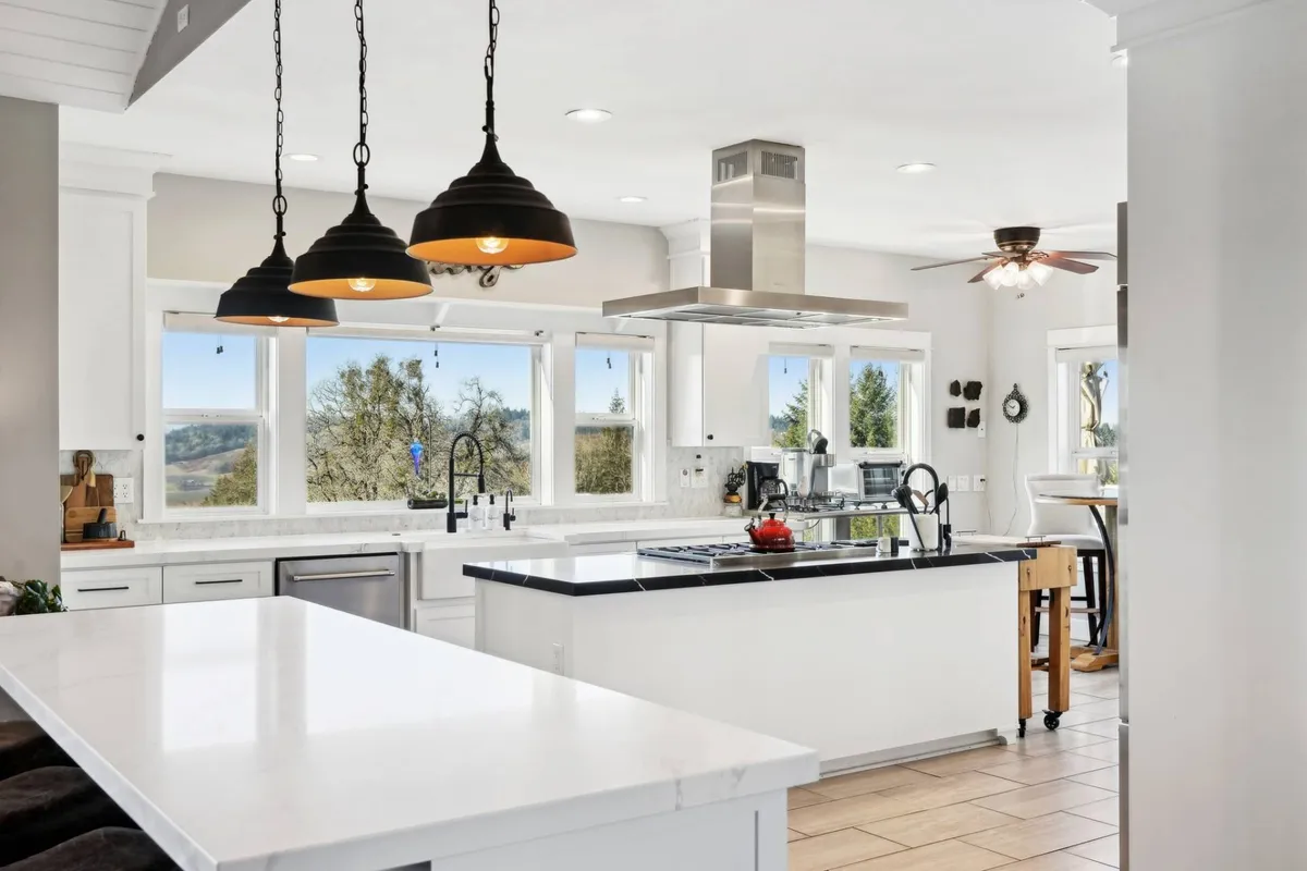 A bright, modern kitchen interior featuring a large island, sleek appliances, and windows that let in natural light and offer views out to the surrounding landscape. The spacious layout is perfect for culinary enthusiasts looking to prepare meals using local finds from the day's vineyard and winery adventures.