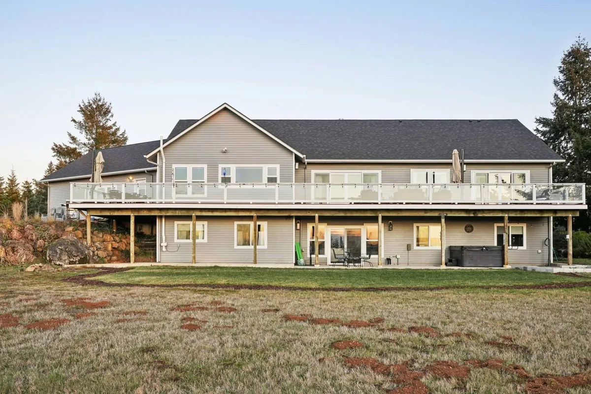 An inviting exterior view of a large deck with comfortable seating, framed by extensive landscaped yard and mature trees. The large windows visually connect the deck to the interior living spaces, while the expansive outdoor area encourages activities like outdoor dining or relaxing with a glass of local wine.