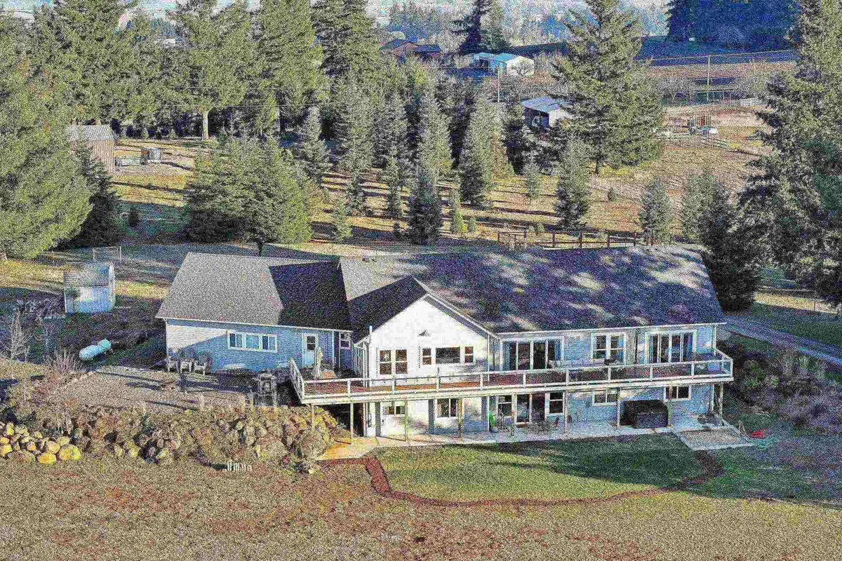 This exterior image showcases a spacious deck bordered by large windows and surrounded by lush trees. The deck extends into the natural landscape, suggesting a seamless connection between indoor comfort and the outdoors, perfect for taking in sunset views over the Van Duzer Corridor after a day of local exploration.
