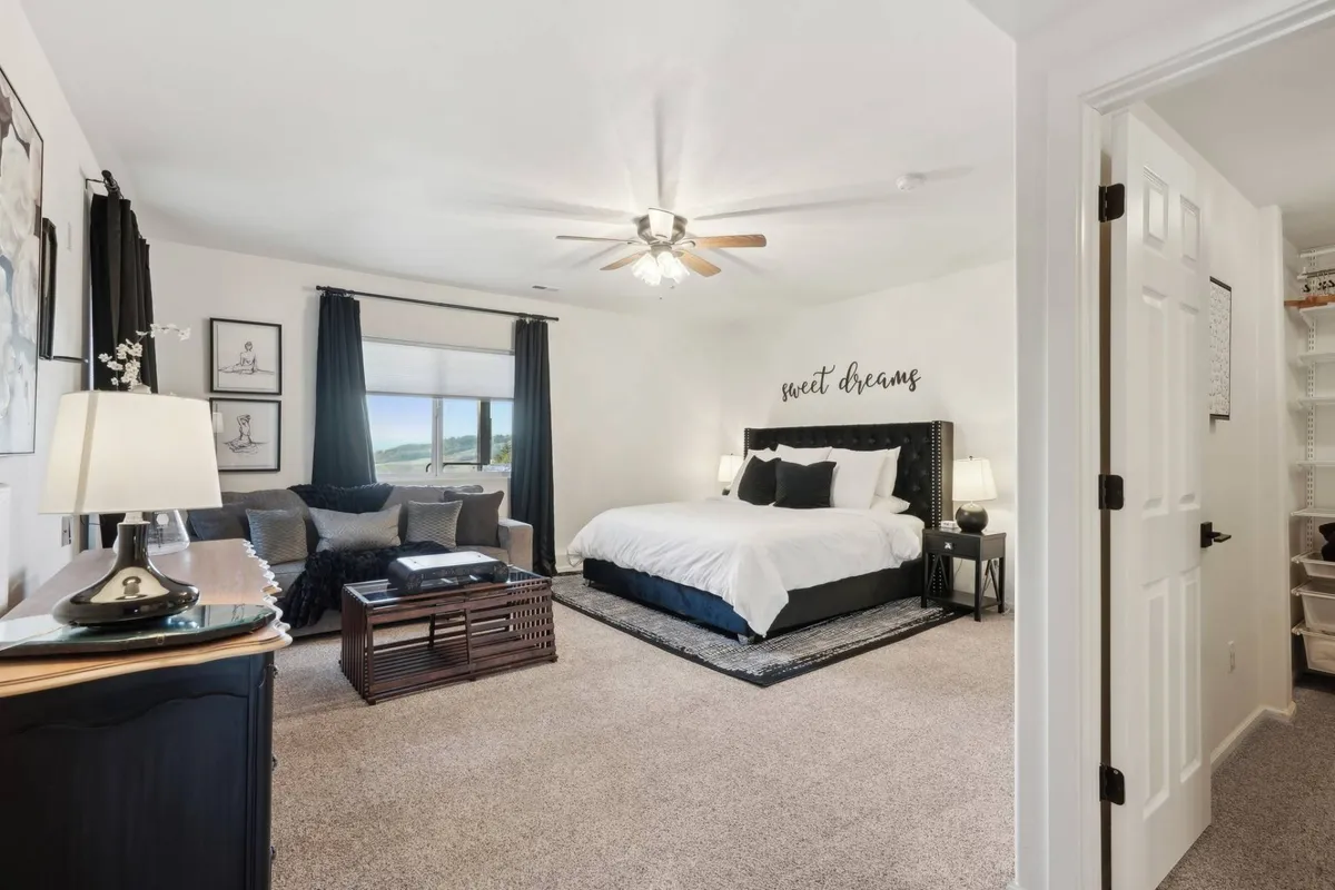 A tranquil bedroom with a large bed adorned with decorative pillows, a cozy seating area with armchairs, tasteful wall art, and a nightstand with a lamp. Soft natural light fills the space, creating a welcoming retreat.