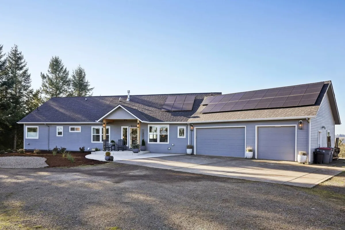 This exterior image features the home's inviting front porch, solar panels, a beautifully landscaped yard, and visible garage doors. The scene conveys a sense of arrival and frames the property within its rural landscape, suggesting a welcoming atmosphere for group gatherings and outdoor enjoyment.