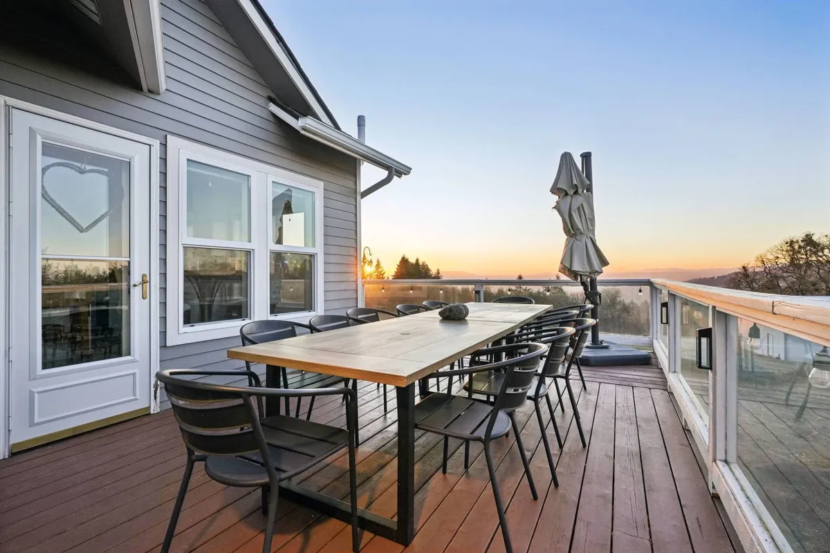 An expansive outdoor dining area features a large table and chairs beneath a parasol, set against a backdrop of a glowing sunset. The arrangement is perfect for alfresco meals and gatherings, with panoramic valley views stretching into the distance.