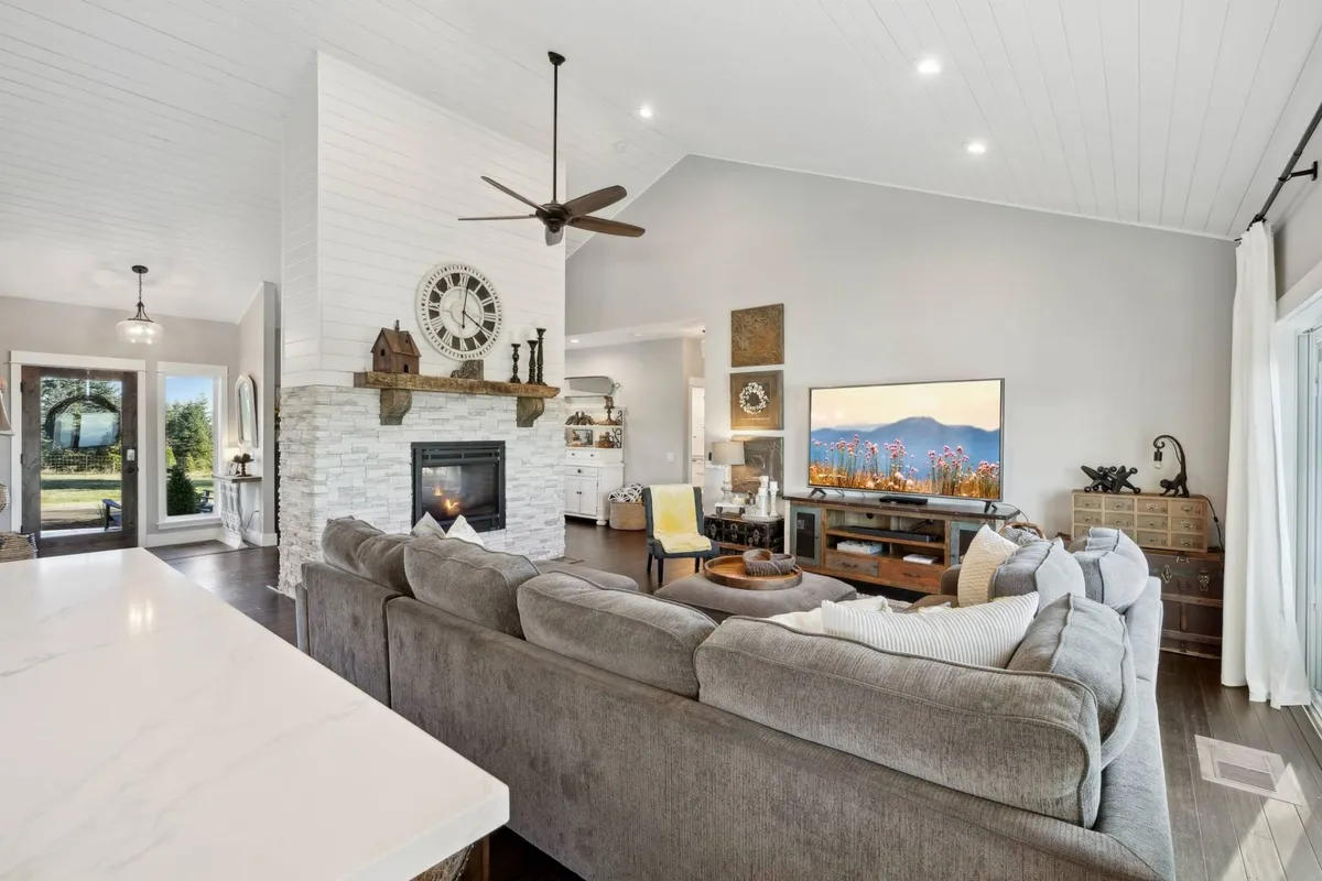 An elegant living room with a large sectional sofa, fireplace, television, dining area, and oversized windows. The fireplace draws the eye and sets a cozy, welcoming tone, while the open layout ensures everyone feels connected whether dining, relaxing, or entertaining.