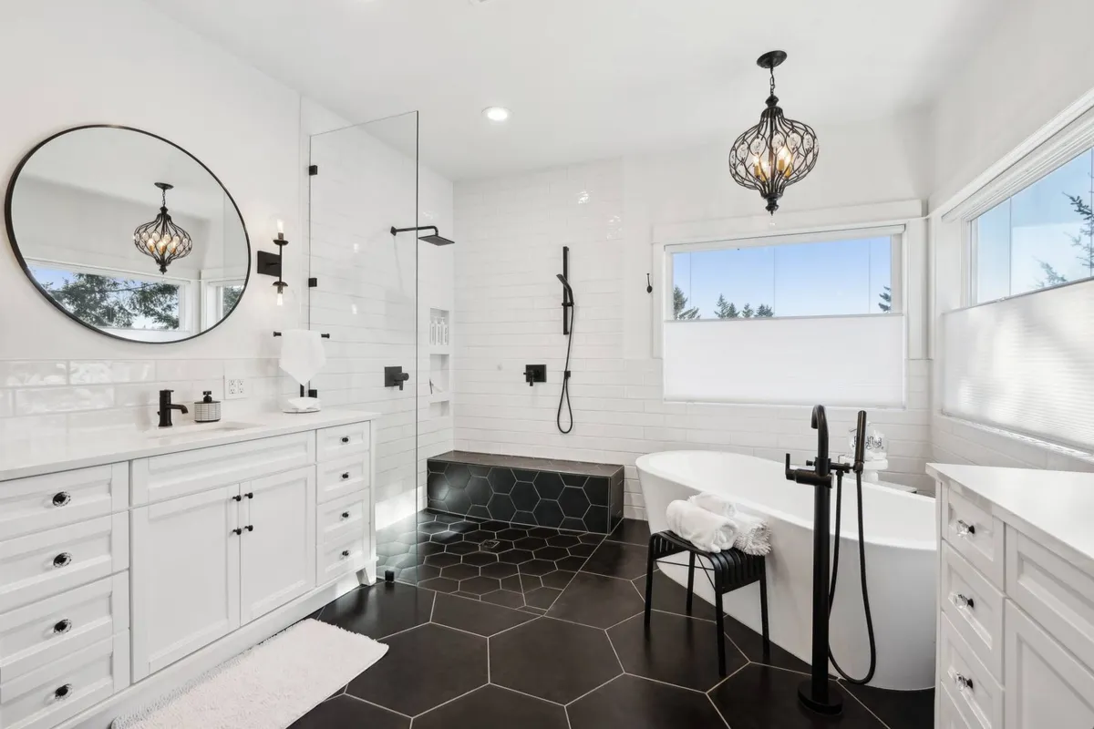 A luxurious spa-inspired bathroom with a freestanding soaking tub as the focal point, hexagonal tile flooring, a large round mirror, and a chandelier overhead. The space exudes calm and relaxation, perfect for a private retreat.