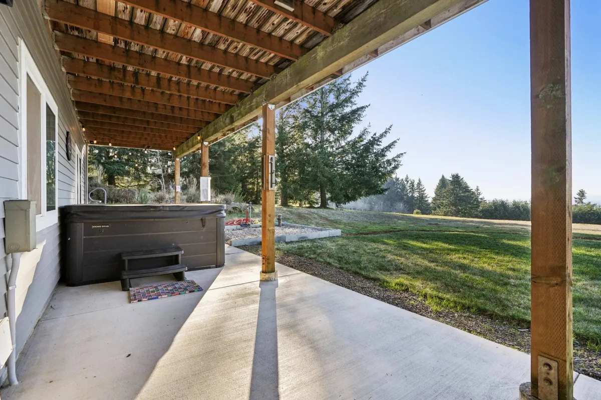 A bubbling hot tub sits beneath sturdy wooden beams, surrounded by lush green grass, offering a tranquil and secluded spot for relaxation. The scene invites you to unwind while soaking in natural beauty, with hints of open sky above for stargazing or morning sunshine.